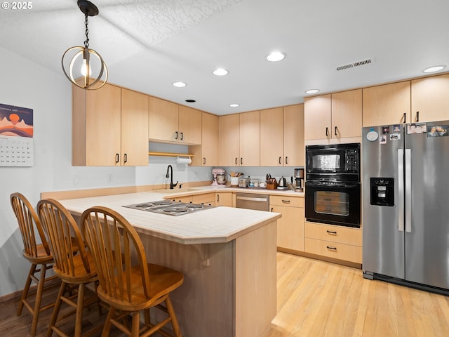 kitchen with a peninsula, black appliances, and light brown cabinets