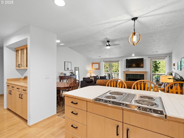 kitchen featuring open floor plan, stainless steel electric stovetop, tile countertops, and light brown cabinets