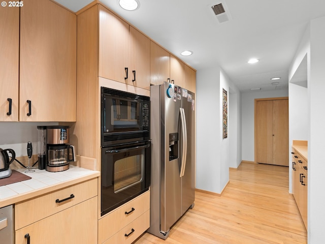 kitchen featuring tile countertops, black appliances, light brown cabinets, and visible vents