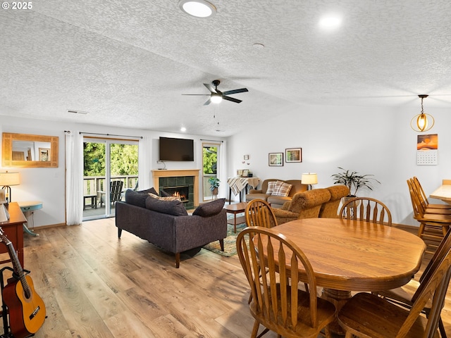 dining space with light wood finished floors, visible vents, a tile fireplace, lofted ceiling, and a textured ceiling