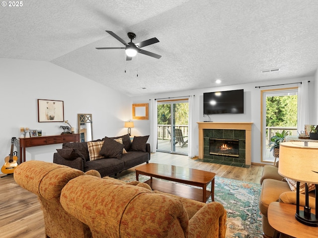 living room with lofted ceiling, visible vents, wood finished floors, and a tile fireplace