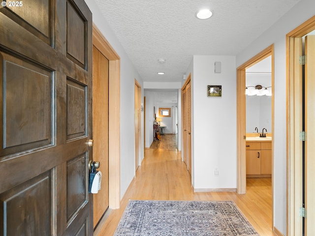 corridor with a sink, light wood-style flooring, baseboards, and a textured ceiling