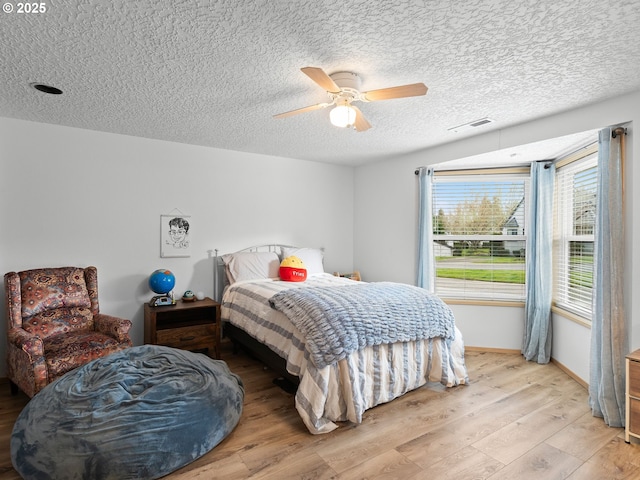 bedroom featuring baseboards, visible vents, a ceiling fan, light wood-style flooring, and a textured ceiling