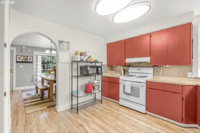 2472 Willamina Ave, Forest Grove, OR 97116 - kitchen with white range with gas stovetop, arched walkways, ventilation hood, tasteful backsplash, and light countertops