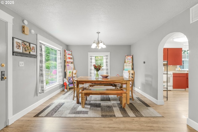 2472 Willamina Ave, Forest Grove, OR 97116 - dining space with light wood-type flooring, a chandelier, arched walkways, baseboards, and a textured ceiling
