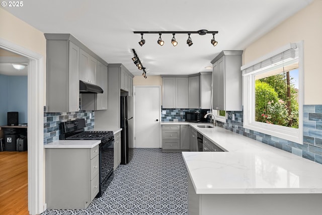 4545 SW Poplar Ln, Portland, OR 97225 - kitchen with gray cabinetry, black appliances, under cabinet range hood, and decorative backsplash