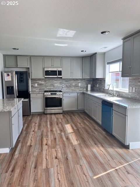 17095 SE Manley St, Portland, OR 97236 - kitchen featuring appliances with stainless steel finishes, gray cabinetry, a sink, decorative backsplash, and light wood finished floors