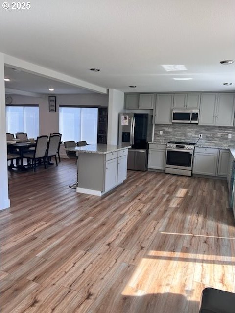 17095 SE Manley St, Portland, OR 97236 - kitchen with stainless steel appliances, gray cabinets, light stone countertops, wood finished floors, and a center island