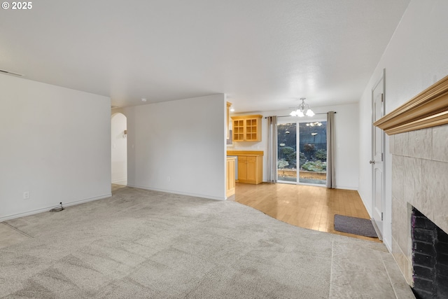 unfurnished living room featuring a tiled fireplace, light carpet, and a chandelier