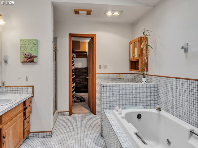 full bath featuring a walk in closet, a jetted tub, a shower stall, and vanity