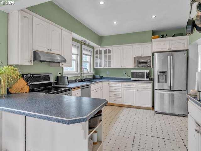 kitchen featuring under cabinet range hood, a sink, dark countertops, appliances with stainless steel finishes, and white cabinets