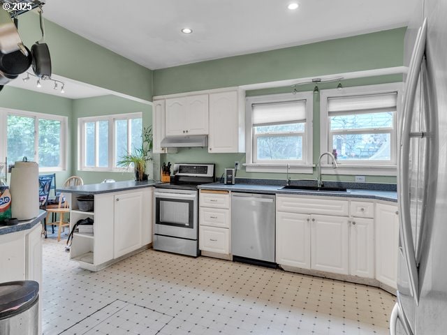 kitchen with light floors, a sink, appliances with stainless steel finishes, white cabinetry, and dark countertops