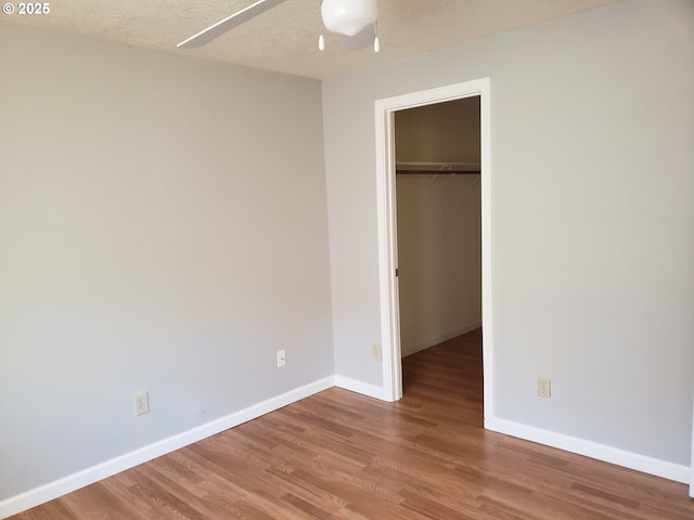 unfurnished bedroom with a walk in closet, a textured ceiling, ceiling fan, hardwood / wood-style flooring, and a closet