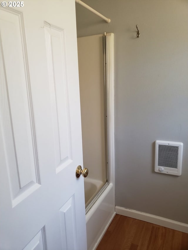 bathroom featuring hardwood / wood-style flooring, bath / shower combo with glass door, and heating unit