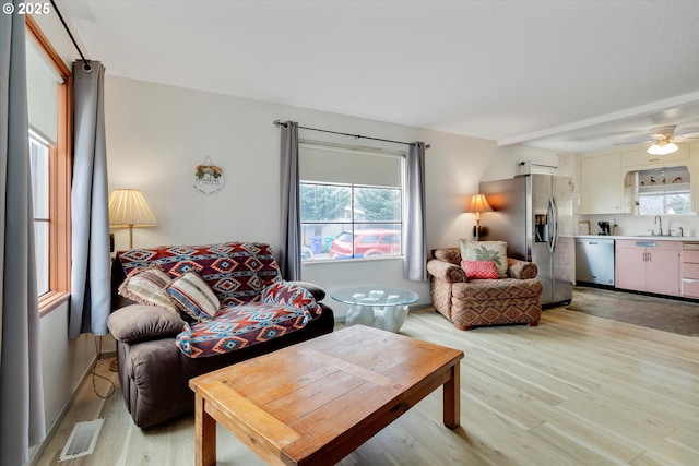 living area with a wealth of natural light, visible vents, light wood-type flooring, and ceiling fan