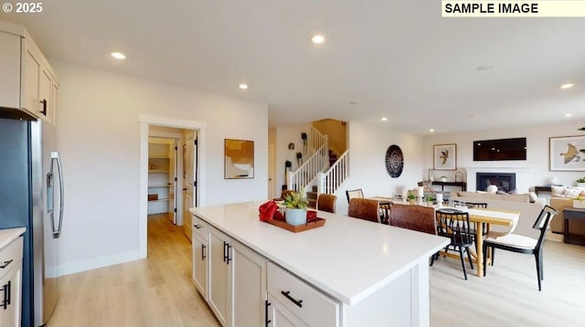 kitchen featuring white cabinets, stainless steel refrigerator with ice dispenser, a center island, and light wood-type flooring