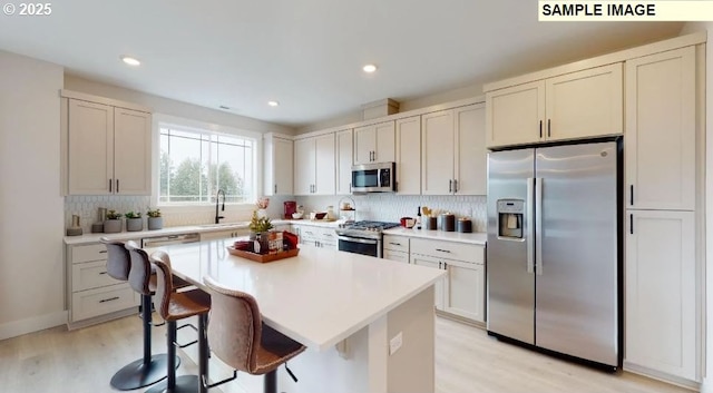 kitchen with sink, stainless steel appliances, light hardwood / wood-style flooring, a kitchen bar, and a kitchen island