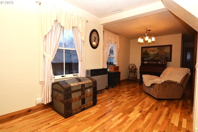 living area with baseboards, wood finished floors, visible vents, and a notable chandelier