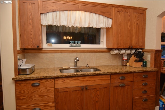 kitchen with backsplash, a sink, light stone countertops, and brown cabinets