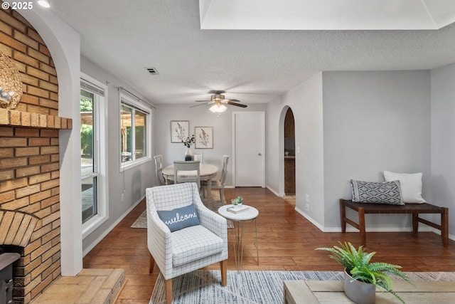 living area with ceiling fan, arched walkways, a textured ceiling, and wood-type flooring