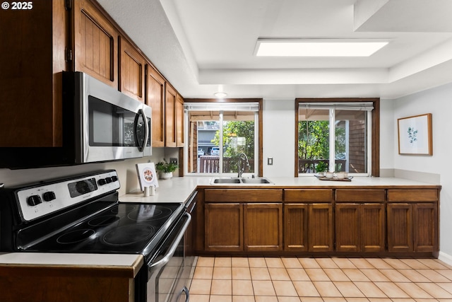 kitchen featuring a sink, a tray ceiling, stainless steel appliances, light countertops, and light tile patterned floors