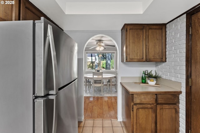 kitchen with ceiling fan, light countertops, light tile patterned floors, freestanding refrigerator, and a raised ceiling