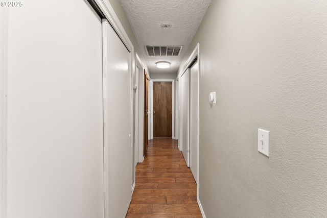 hall with visible vents, a textured ceiling, wood finished floors, and a textured wall