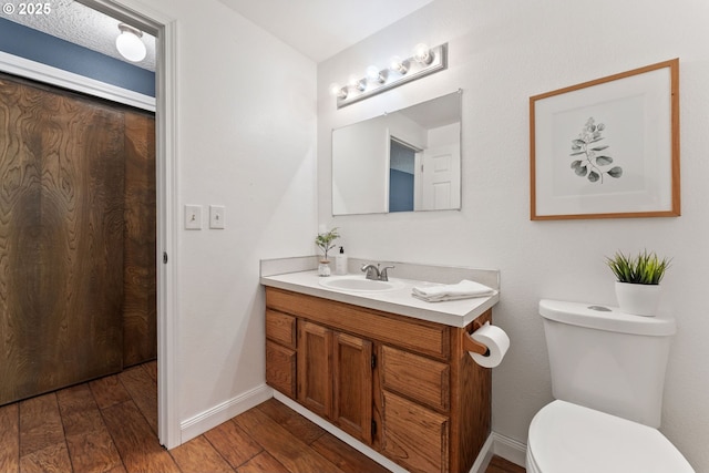 bathroom featuring toilet, vanity, baseboards, and wood finished floors