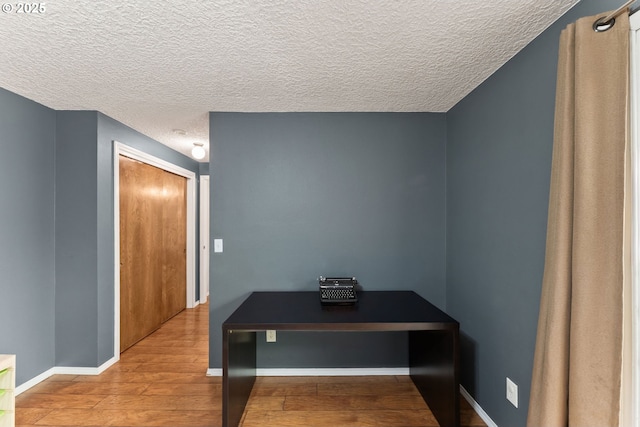 hallway featuring a textured ceiling, baseboards, and wood finished floors