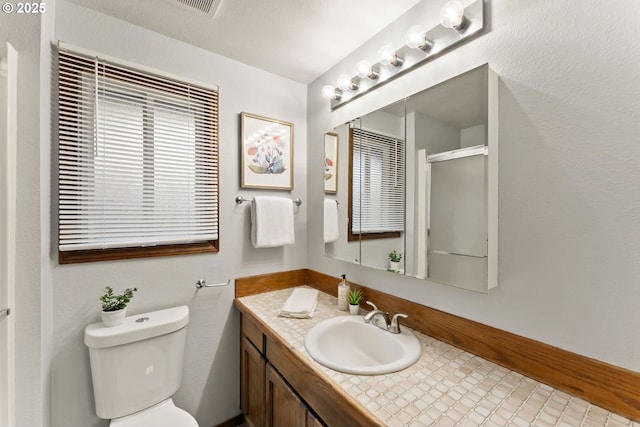 bathroom featuring toilet, vanity, and a shower with shower door