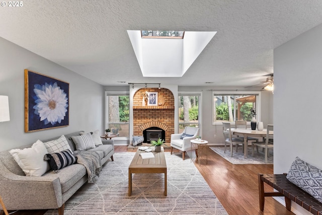 living area featuring a textured ceiling, wood finished floors, a skylight, a fireplace, and baseboards