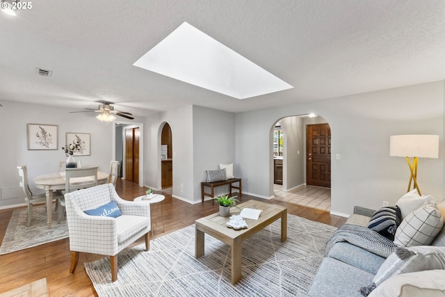 living area with visible vents, baseboards, light wood-type flooring, arched walkways, and a ceiling fan