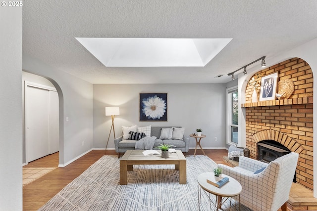 living area featuring arched walkways, a textured ceiling, a skylight, and wood finished floors