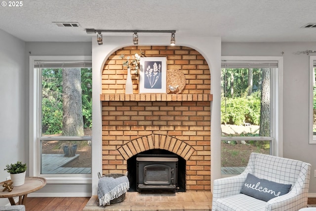 living area with a wealth of natural light, visible vents, wood finished floors, and a wood stove