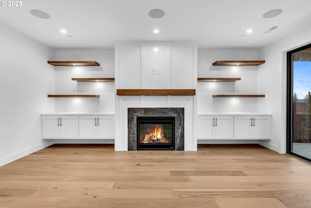 unfurnished living room with a high end fireplace, light wood-style floors, baseboards, and visible vents