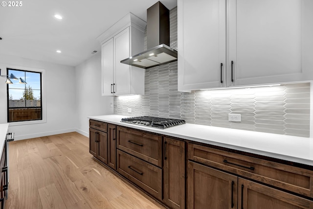 kitchen featuring baseboards, wall chimney exhaust hood, white cabinetry, stainless steel gas stovetop, and recessed lighting