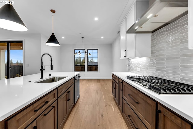 kitchen featuring wall chimney range hood, light countertops, white cabinets, appliances with stainless steel finishes, and a sink