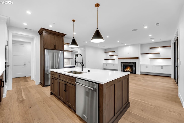 kitchen featuring a sink, light countertops, appliances with stainless steel finishes, dark brown cabinets, and light wood-style flooring