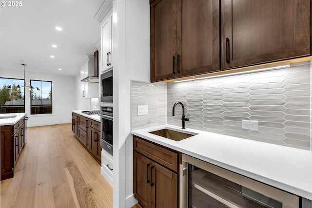 kitchen with oven, a sink, light countertops, light wood-style floors, and beverage cooler