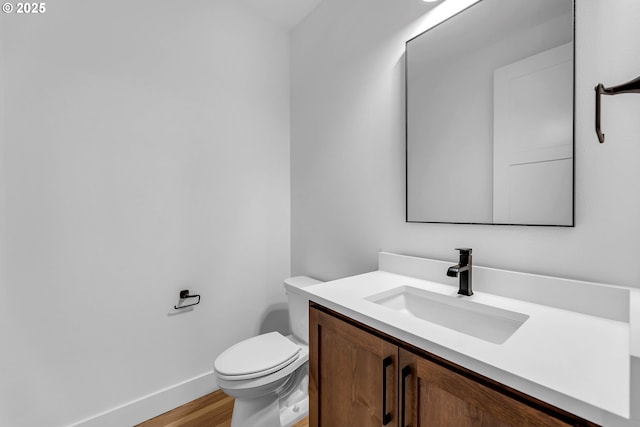 half bath featuring toilet, baseboards, vanity, and wood finished floors