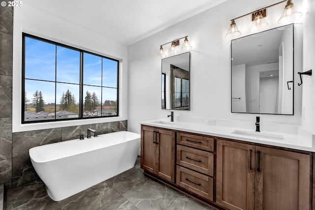 full bathroom with double vanity, marble finish floor, a sink, and a soaking tub