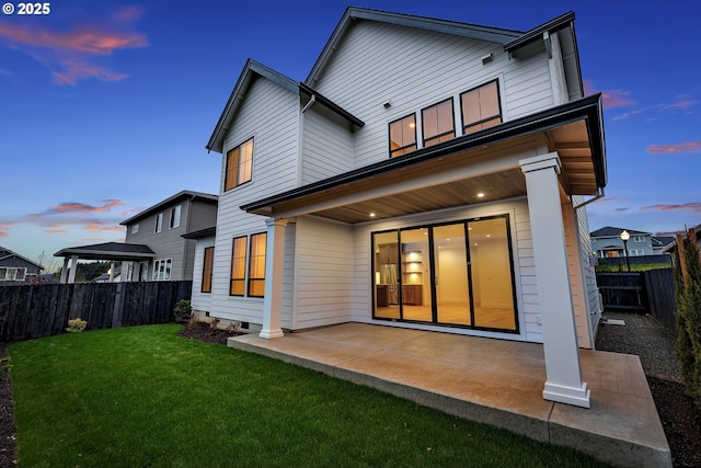 back of property at dusk with a patio area, a fenced backyard, and a lawn
