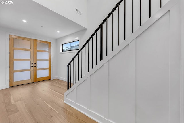 foyer entrance featuring visible vents, baseboards, wood finished floors, stairs, and french doors