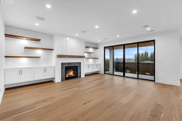 unfurnished living room featuring light wood-type flooring, baseboards, a glass covered fireplace, and recessed lighting