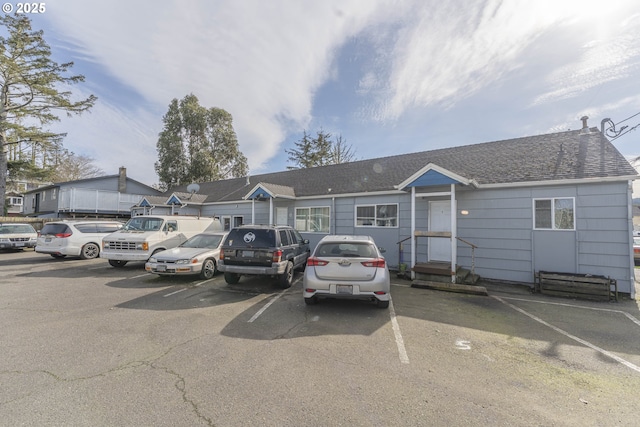 view of front of house with uncovered parking, entry steps, and roof with shingles