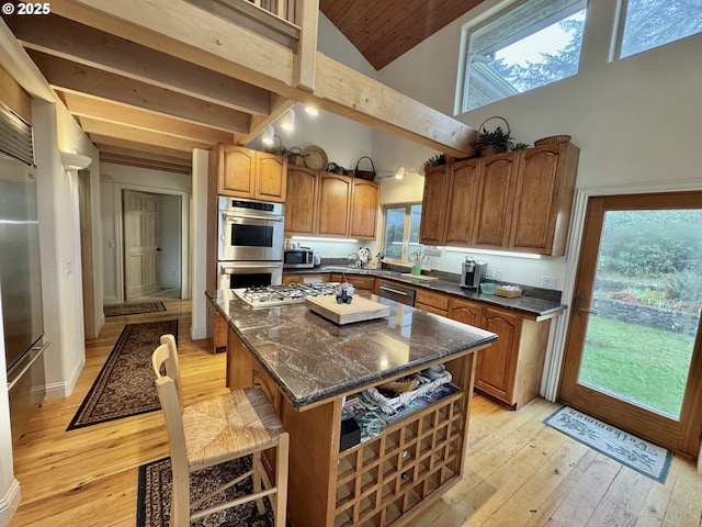 31640 Spruce Dr, Gold Beach, OR 97444 - kitchen with beamed ceiling, brown cabinets, a kitchen island, appliances with stainless steel finishes, and light wood-style floors