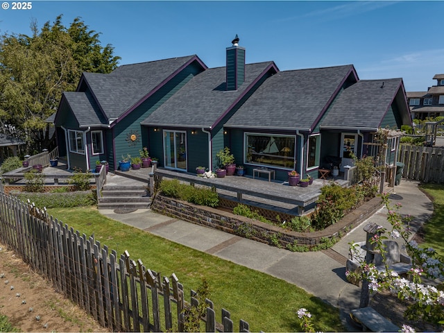 back of property with a chimney, a deck, a fenced backyard, a yard, and a shingled roof