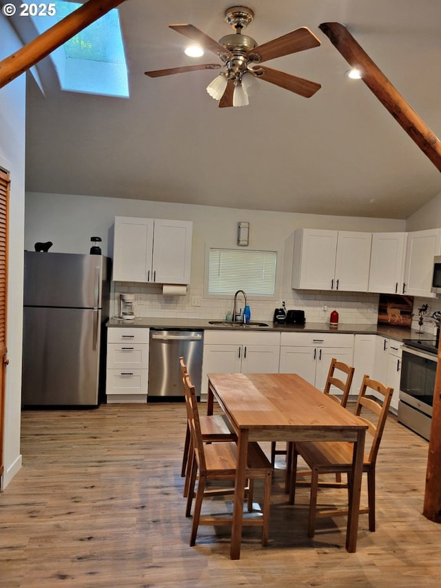 kitchen featuring stainless steel appliances, light wood-style flooring, lofted ceiling with skylight, white cabinetry, and a sink