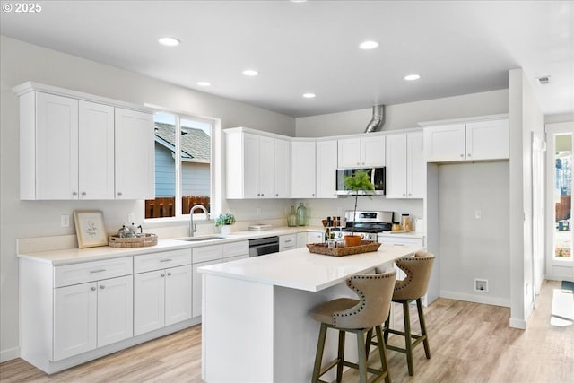 kitchen featuring appliances with stainless steel finishes, sink, white cabinetry, a center island, and a breakfast bar area