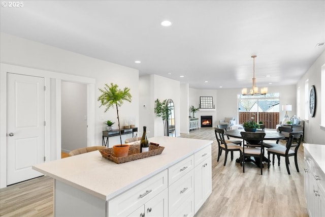 kitchen with hanging light fixtures, white cabinetry, a center island, a notable chandelier, and light hardwood / wood-style floors